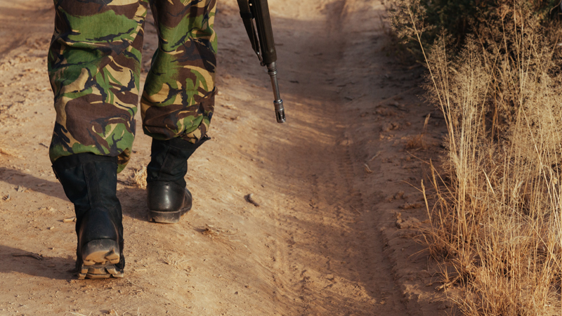 Die Füße eines bewaffneten Soldaten, der auf einem sandigen Feldweg läuft