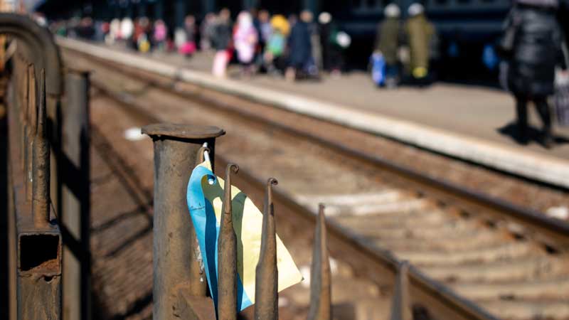 An einem Metallgitter an einem Bahnhof an der ukrainischen Westgrenze hängt eine verwitterte ukrainische Papierflagge.