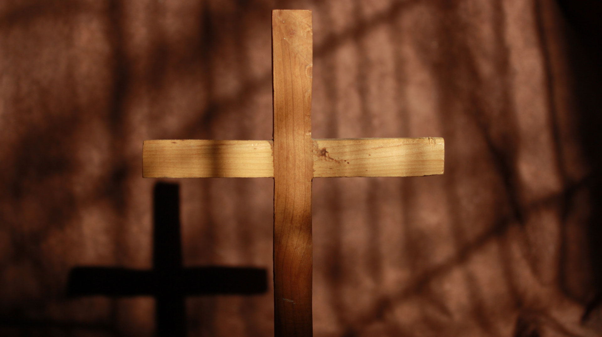 Ein Holzkreuz wirft Schatten auf eine rustikale braune Wand