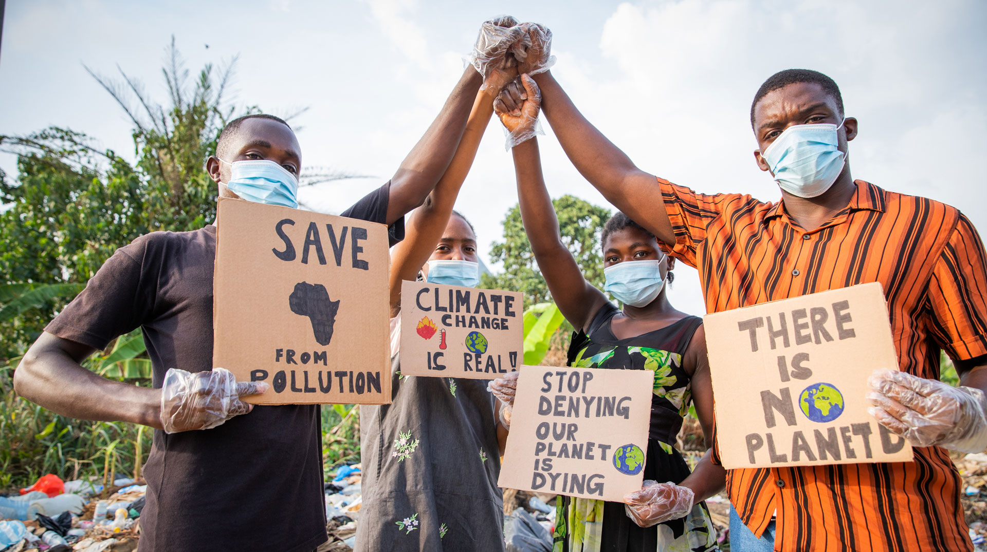 Four young adults protest with signs against pollution outside an illegal open landfill in Africa.