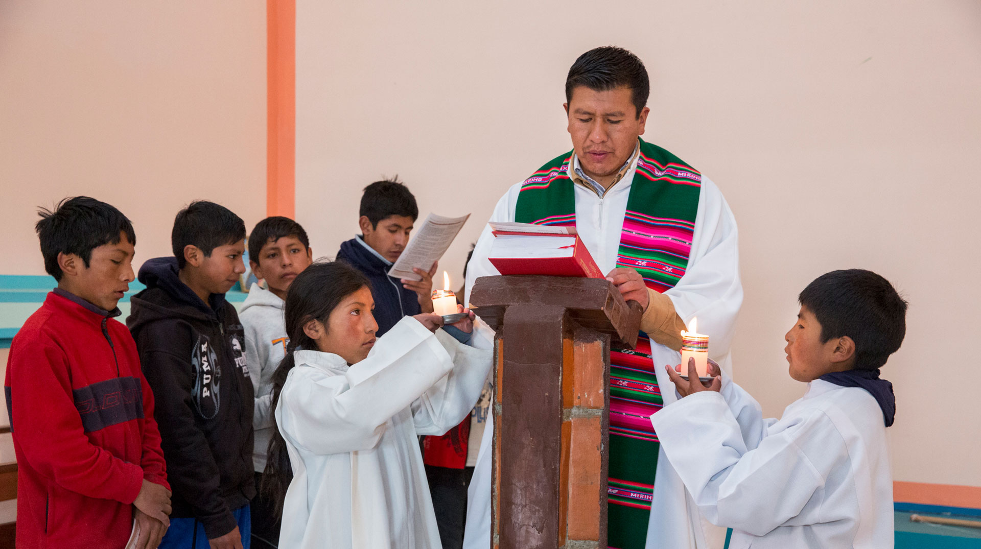 Ein Priester mit bunter Stola steht am Ambo, um ihn herum zahlreiche Kinder, darunter zwei Messdiener.