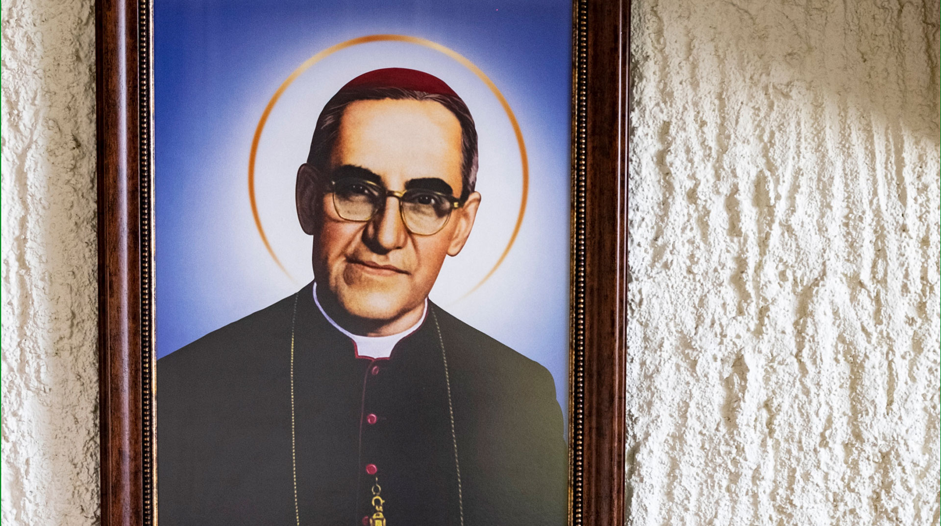 An einer rau verputzten Wand hängt ein Bild des heiligen Óscar Romero mit Heiligenschein.