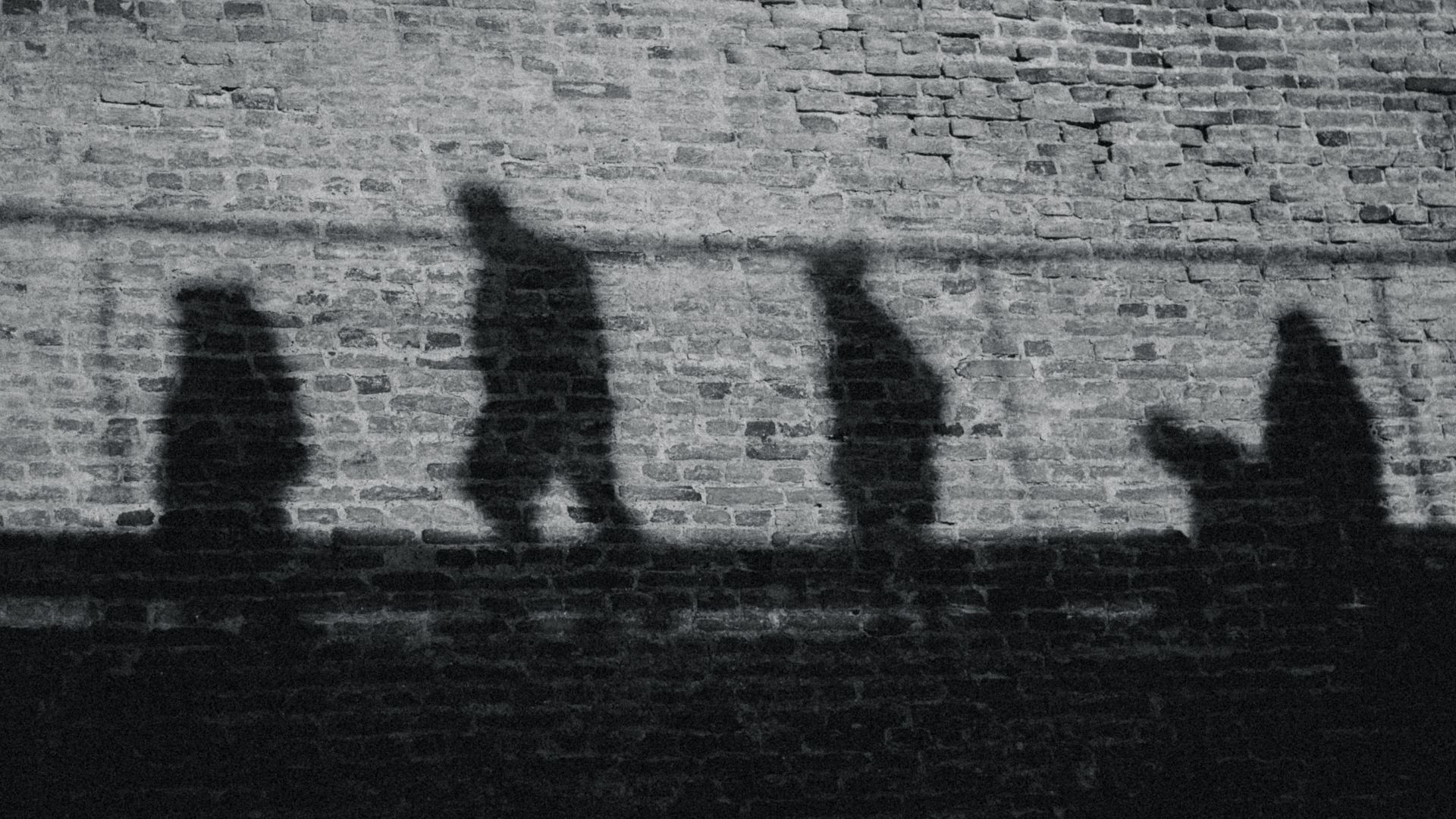 Symbolbild Menschenhandel, Grauzone, Illegalität, Versteck, Schatten: Mehrere Schatten huschen über eine Mauer
