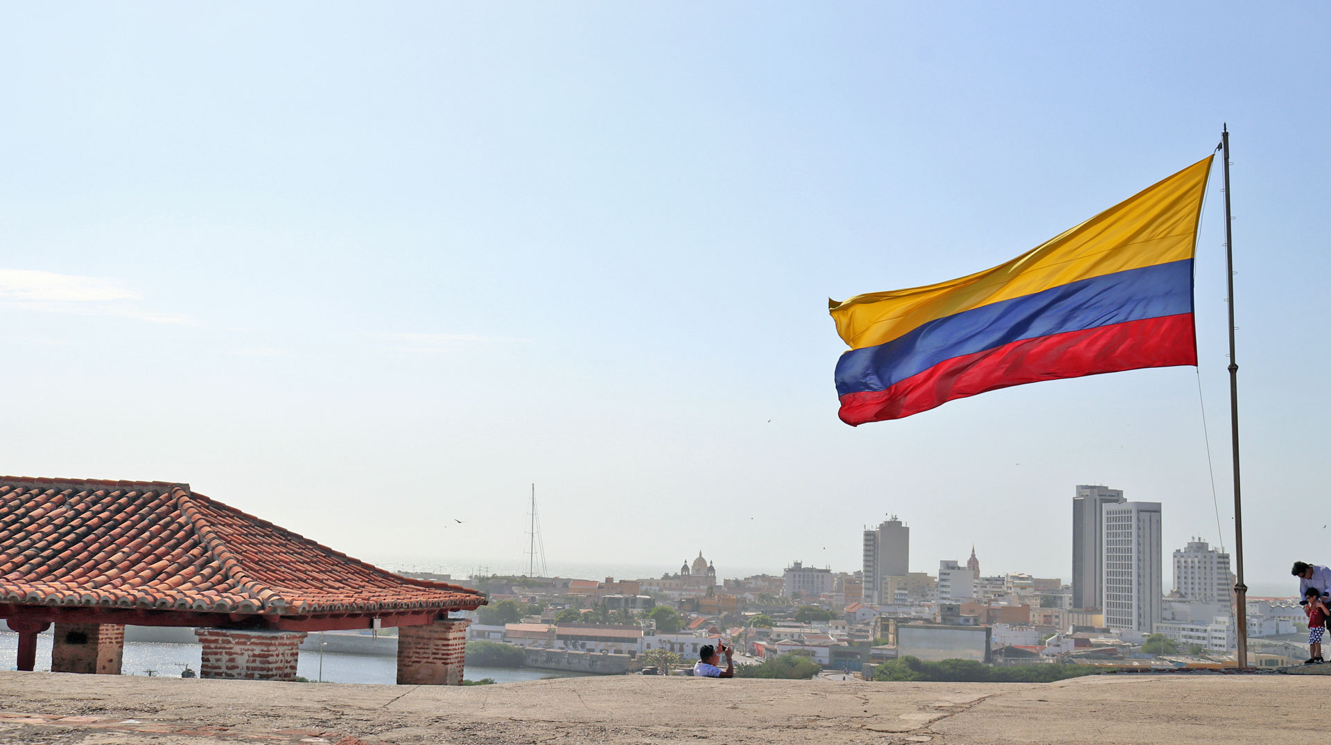 Eine große kolumbianische Nationalflagge weht auf der Festung von Cartagena im Norden Kolumbiens. Im Hintergrund zu sehen ist die Skyline von Cartagena
