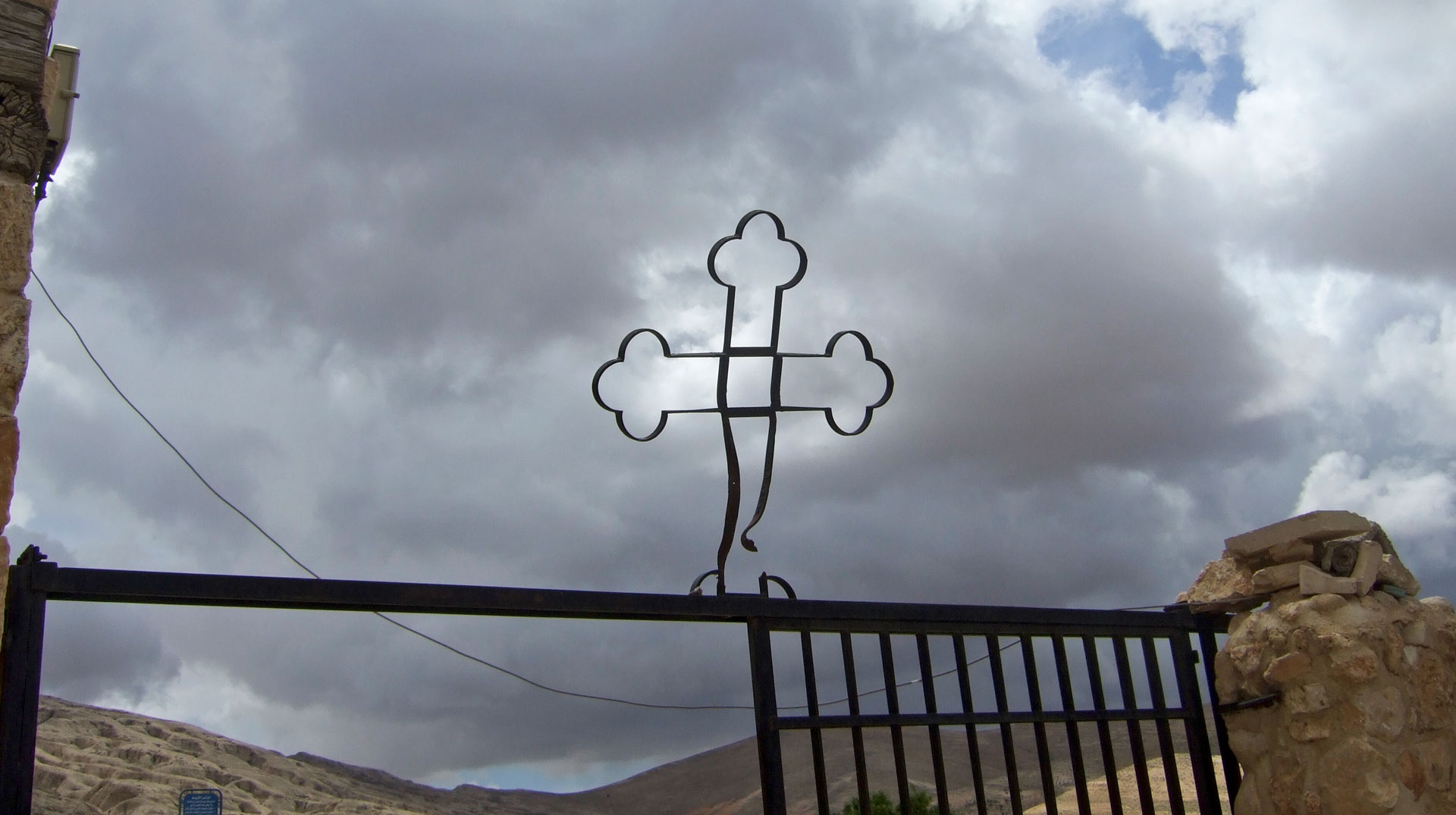 Ein verbogenes Kreuz auf einem Zaun vor düsterem bewölktem Himmel im syrischen Maalula am 12. April 2015.