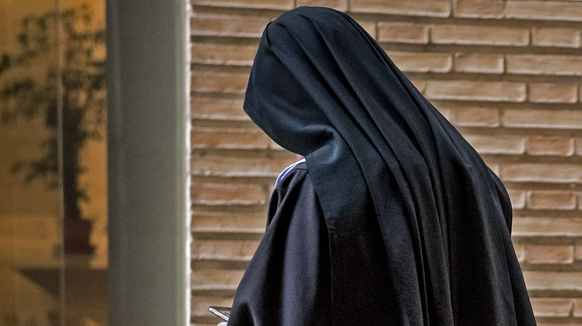 Eine Nonne mit schwarzem Habit und Schleier steht mit gesenktem Kopf