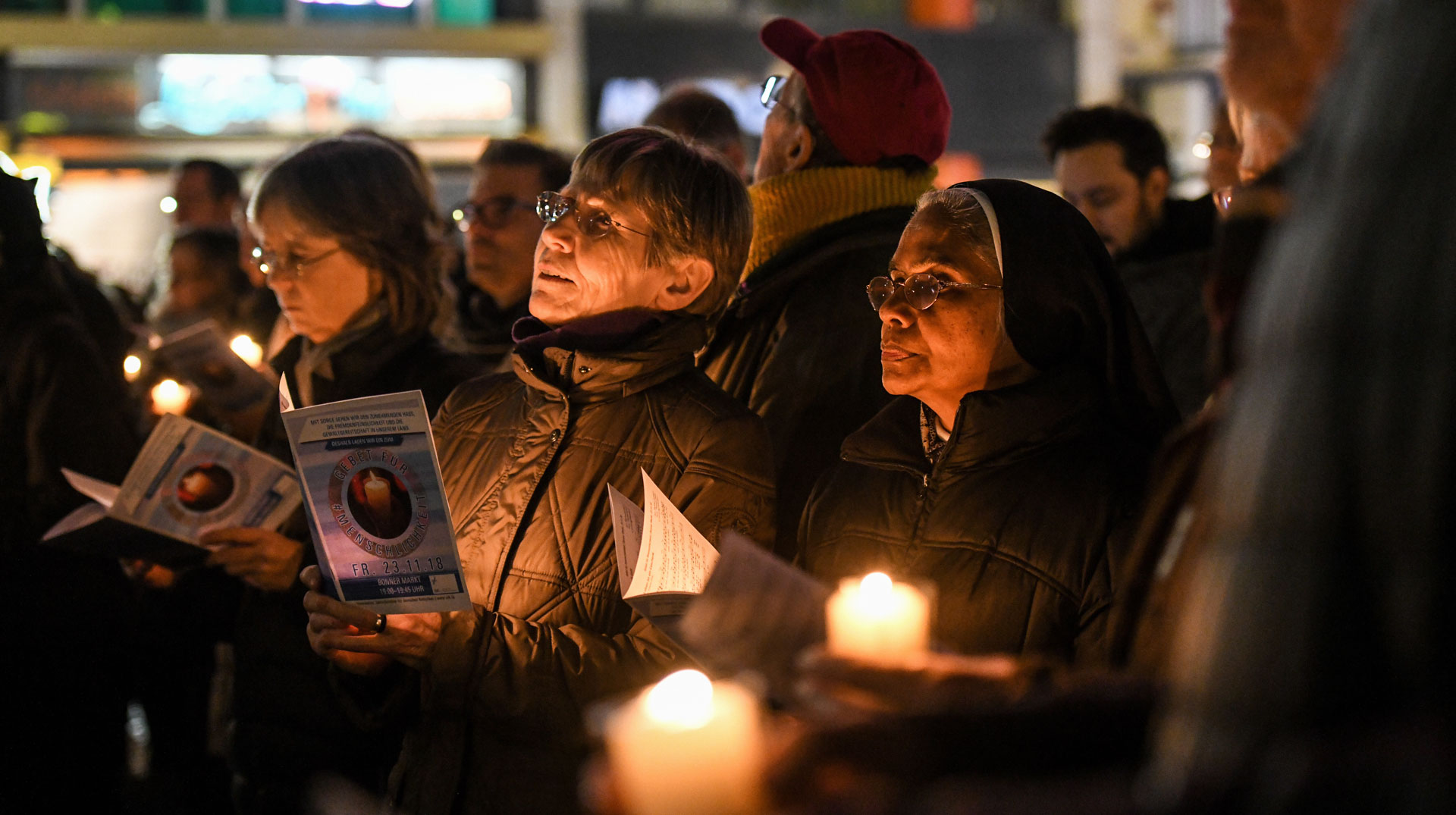 Menschen halten Notenblätter und brennende Kerzen auf dem Bonner Marktplatz am 23. November 2018 bei einem Gebet für Menschlichkeit und Toleranz, zu dem das ZdK eingeladen hat.
