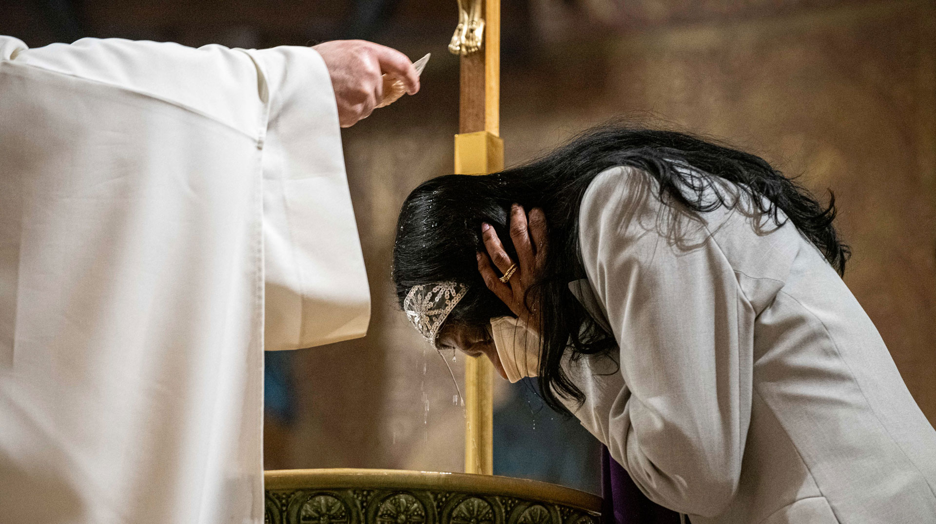 Eine in weiß gekleidete Frau empfängt die Taufe in der Osternacht am 4. April 2021 in der Kirche Saint Pierre in Charenton-le-Pont (Frankreich). Sie bückt sich über das Taufbecken, während ein Priester ihr das Weihwasser über den Kopf gießt.