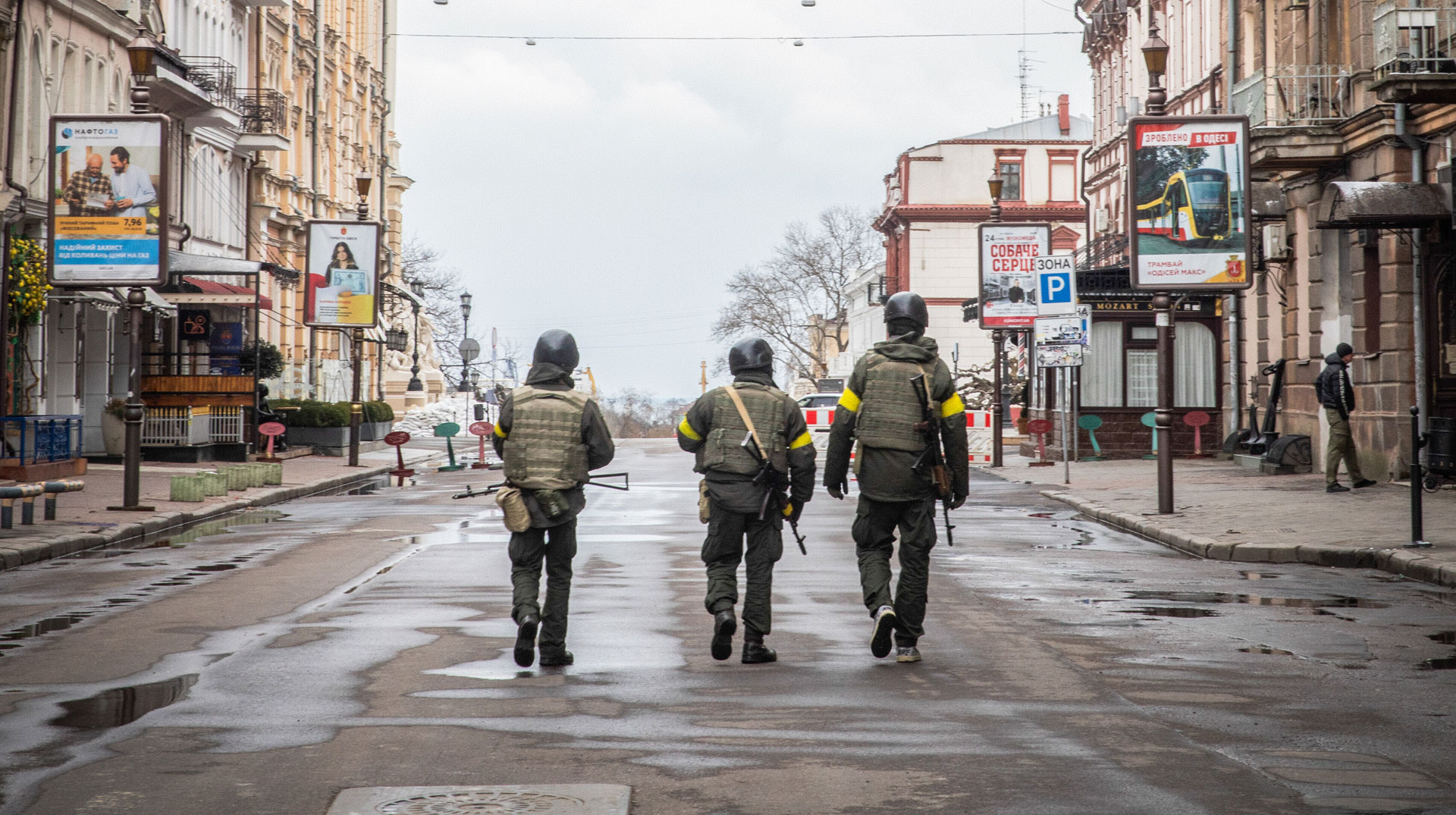 Drei Männer mit Helmen, Waffen und Schutzwesten, ukrainische Freiwillige der Territorialverteidigung, gehen am 9. März 2022 in Odessa (Ukraine) eine menschenleere Straße entlang.