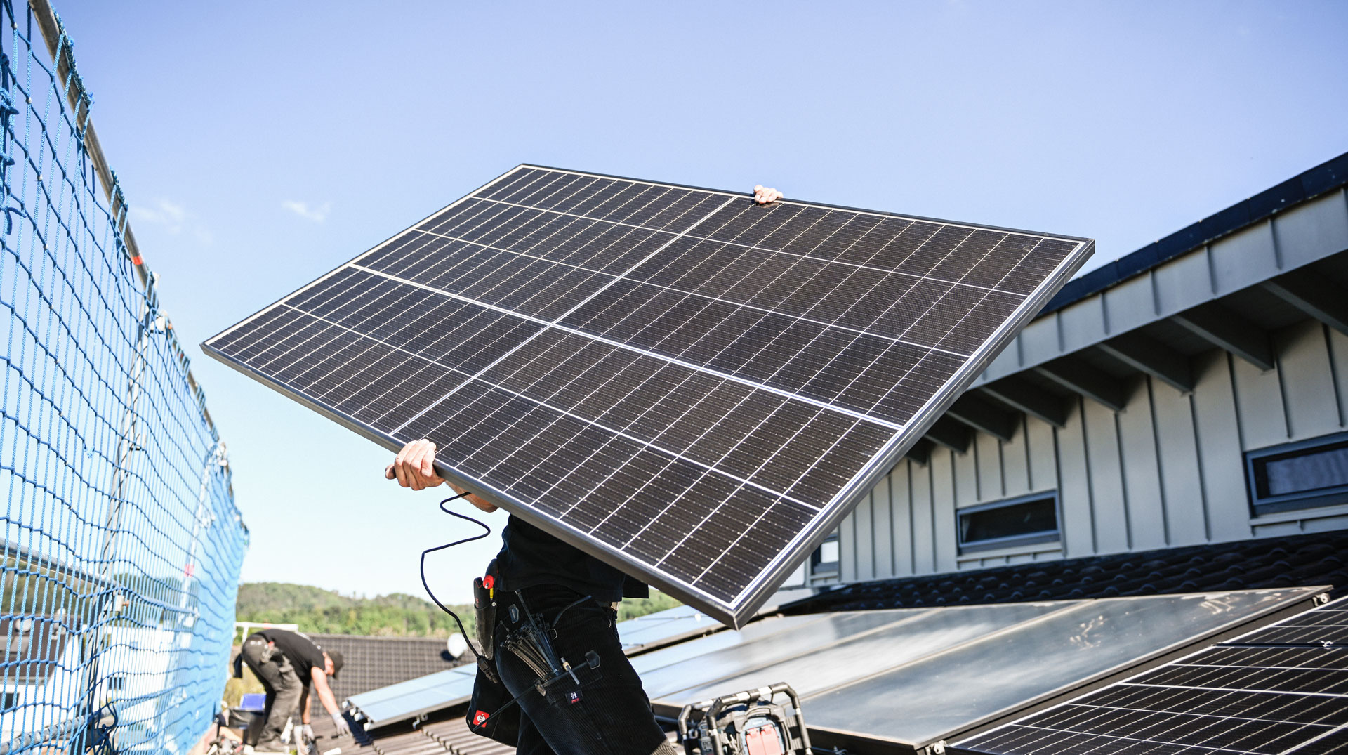 Dachdecker installieren Solarpaneele um eine Solarthermieanlage (m.u.) herum auf dem Dach eines Wohnhauses am 22. September 2022 in Hennef. Ein Dachdecker trägt eine Solarplatte in den Händen.