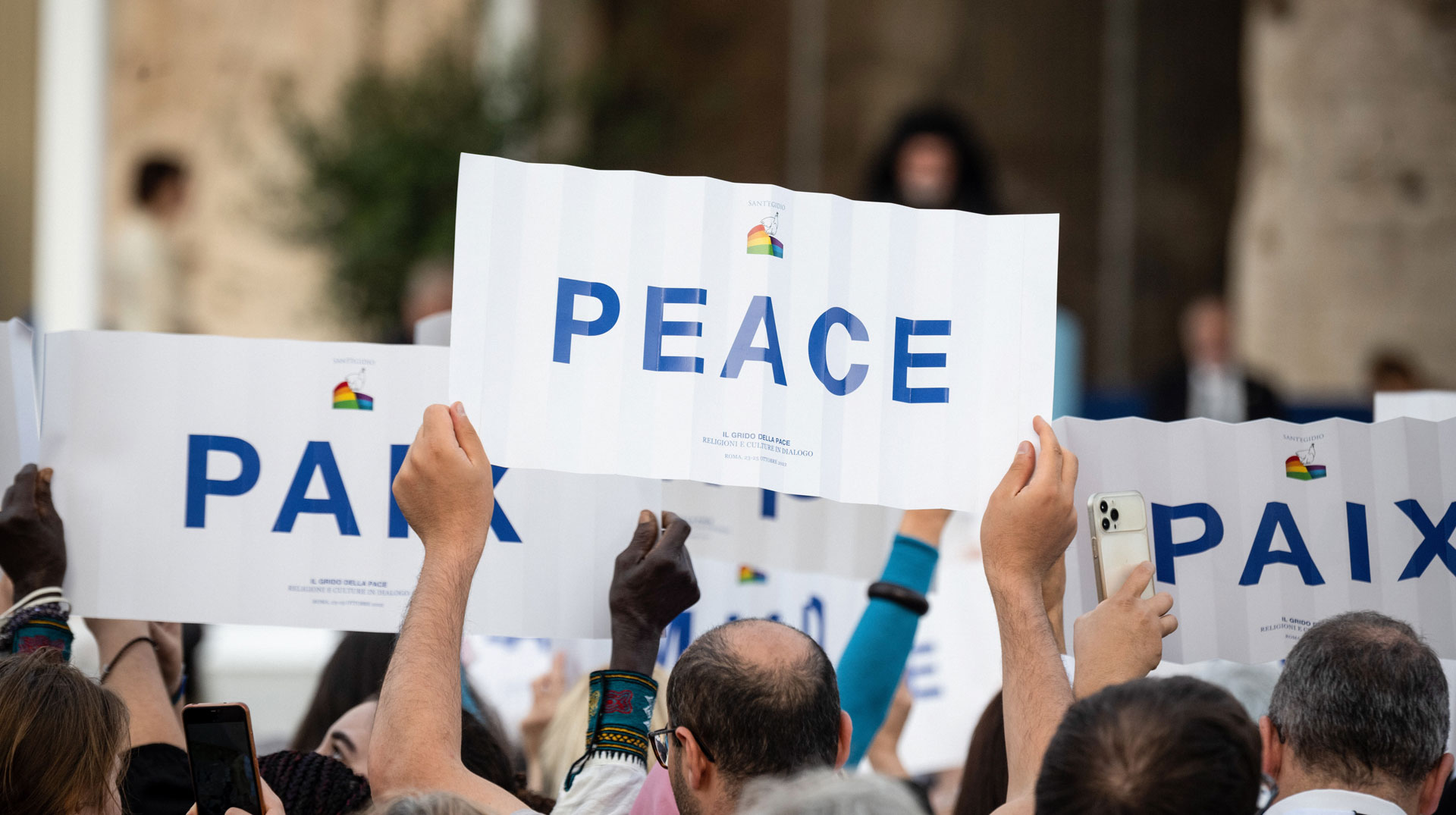 Menschen halten Pappschilder hoch mit dem Wort "Frieden" in verschiedenen Sprachen am 25. Oktober 2022 vor dem Kolosseum in Rom während des internationalen Weltfriedenstreffens der katholischen Gemeinschaft Sant Egidio.