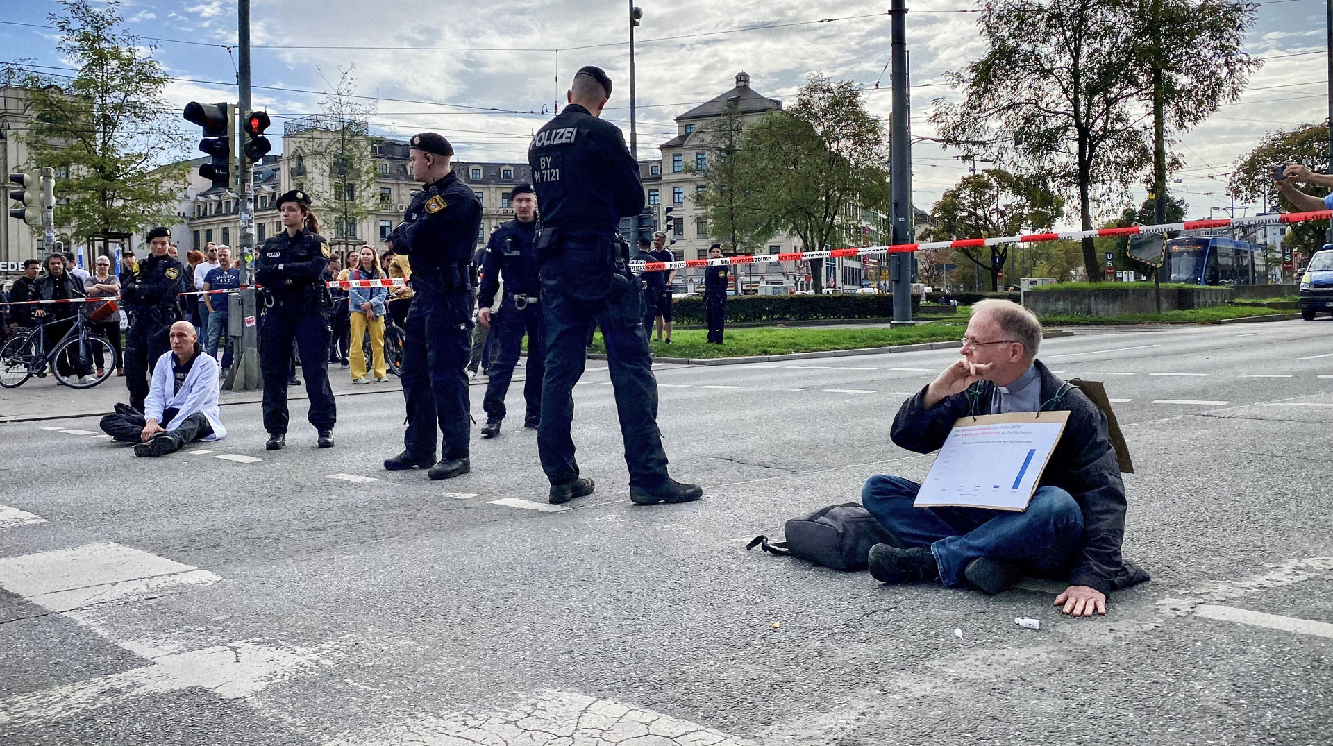 Jörg Alt (r.), Sozialwissenschaftler, Sozialethiker und Migrationssoziologe, bei einer Straßenblockade für eine andere Klimapolitik am 28. Oktober 2022 in München. Polizisten stehen daneben.