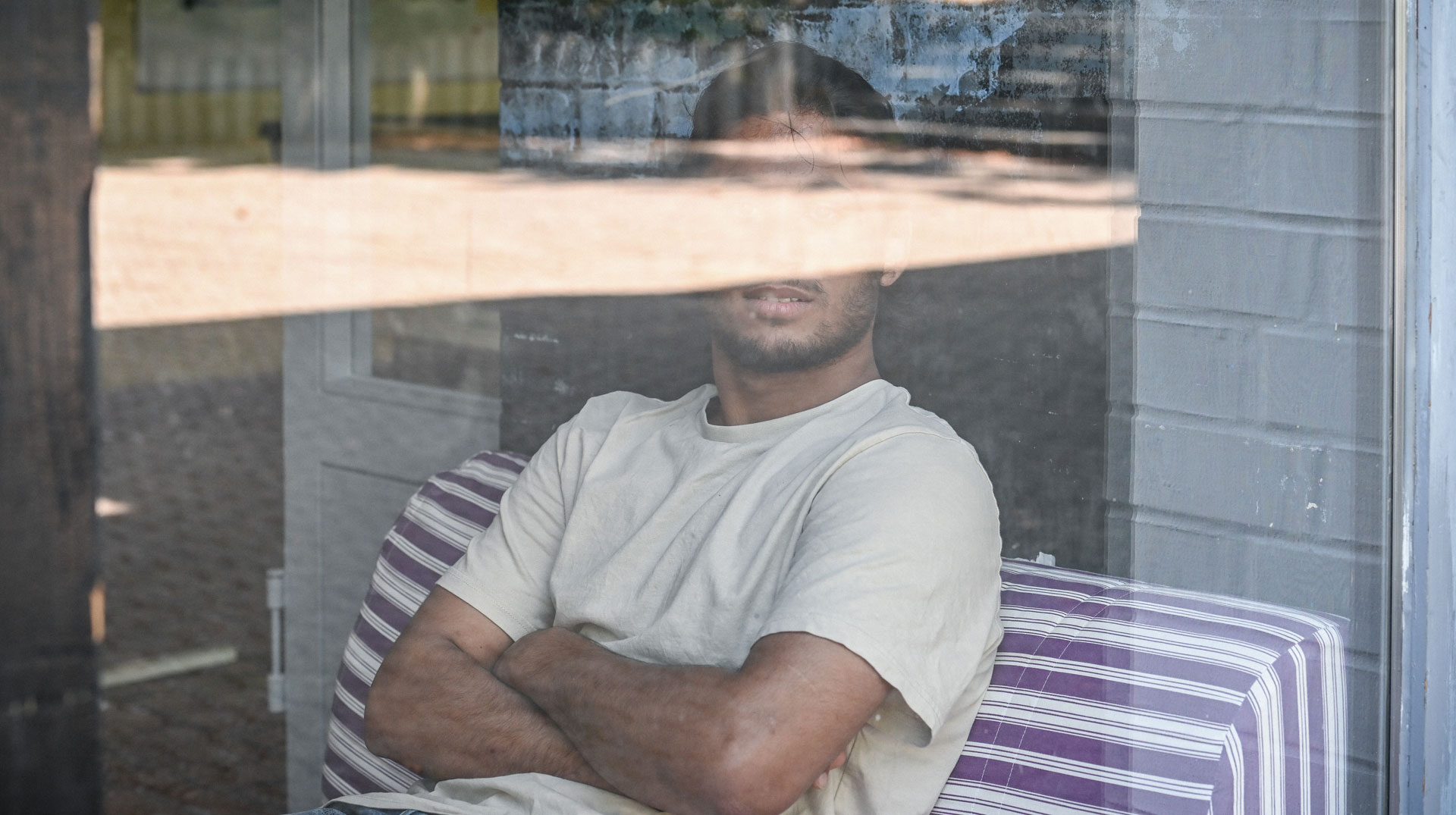 Mohammad, Flüchtling mit Aufenthaltsgenehmigung, sitzt am 12. August 2024 hinter der Glasscheibe eines Gebäudes einer Kirchengemeinde in Bonn. Die Gemeinde hatte ihm Kirchenasyl gewährt.