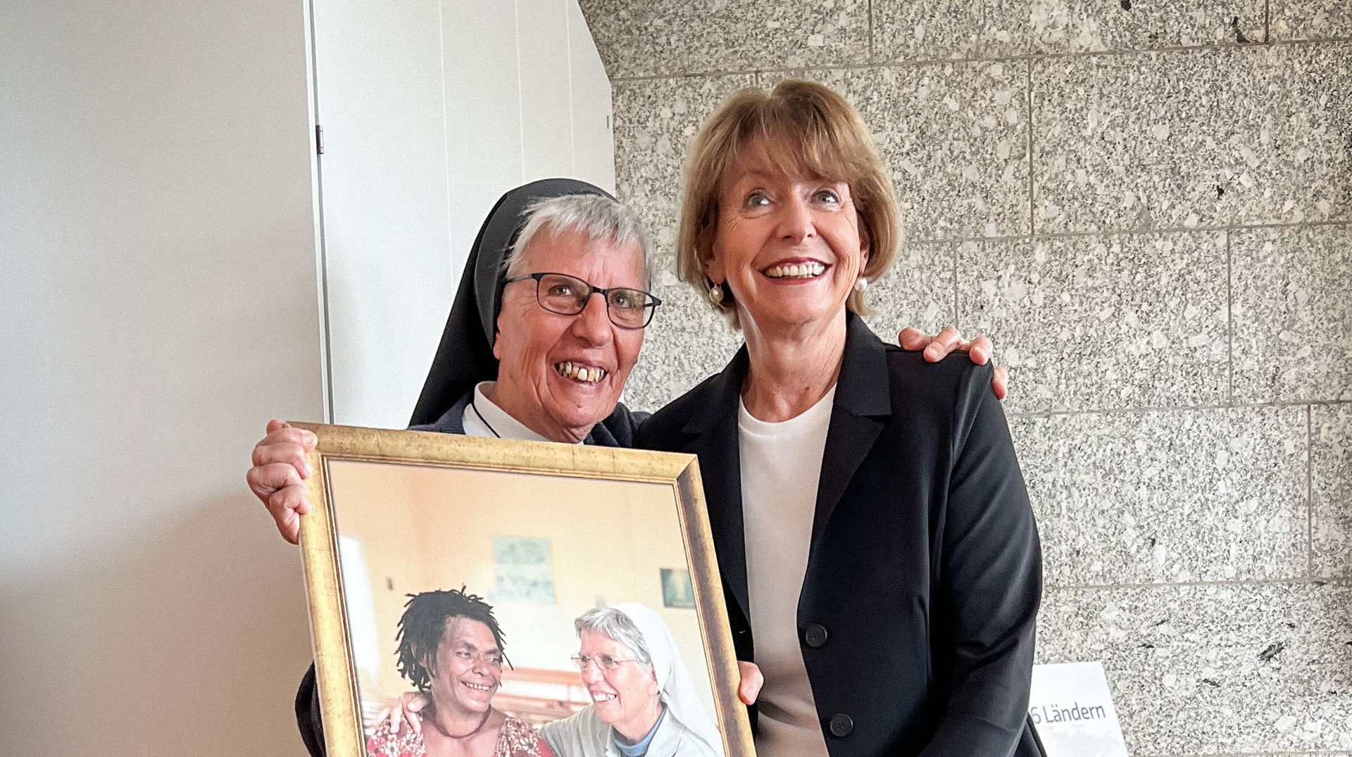 Ordensfrau Schwester Lorena Jenal (l.) und Henriette Reker, Oberbürgermeisterin von Köln, am 7. August 2025 im Kölner Rathaus in Köln. Schwester Lorena hält ein gerahmtes Bild in den Händen, in dem sie eine Frau aus Papua-Neuguinea umarmt.