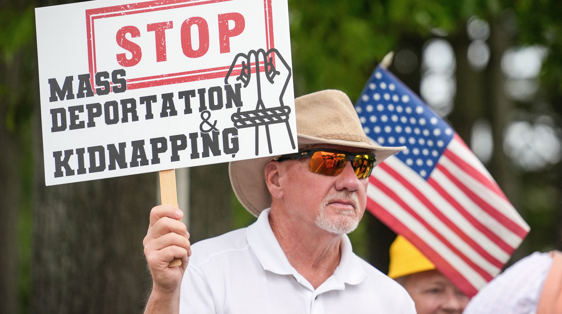 Ein Mann hält ein Schild "Stop Mass Deportation - Kidnapping" (dt. Massenabschiebung stoppen - Entführung)
