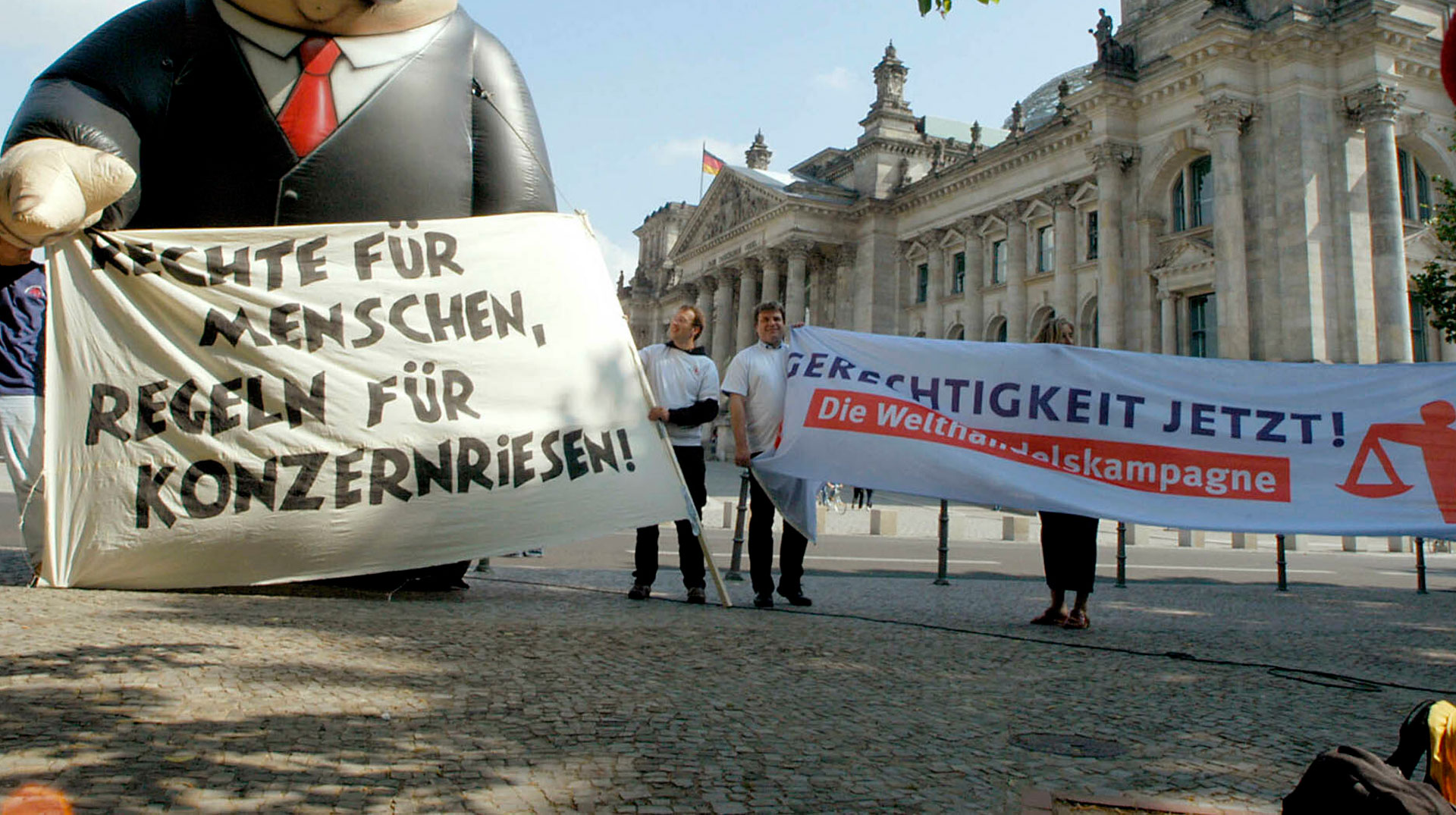 Menschen protestieren vor dem Bundestag mit einem Transparent, auf dem "Rechte für Menschen, Regeln für Konzernriesen" steht.