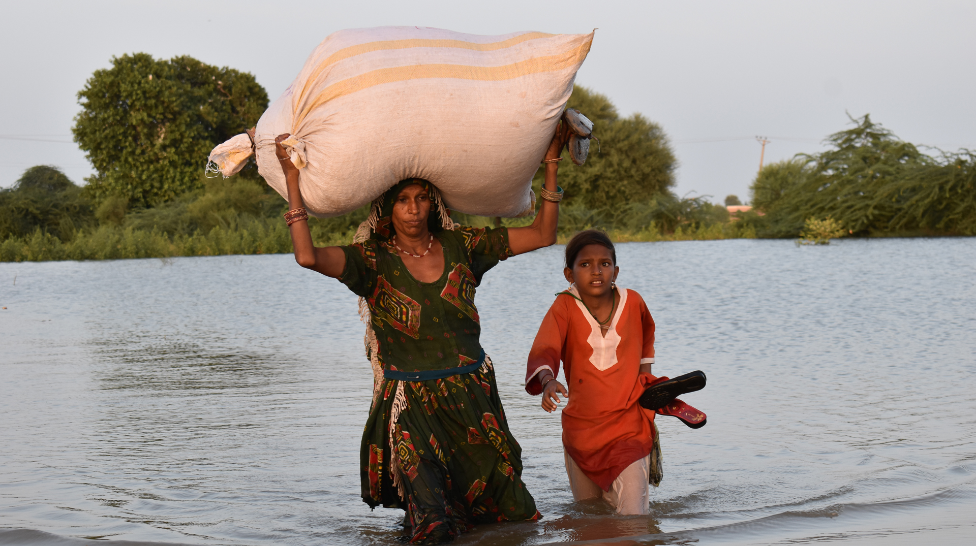 Ein Kind und seine Mutter in Pakistan tragen ihr Hab und Gut durch einen Fluss