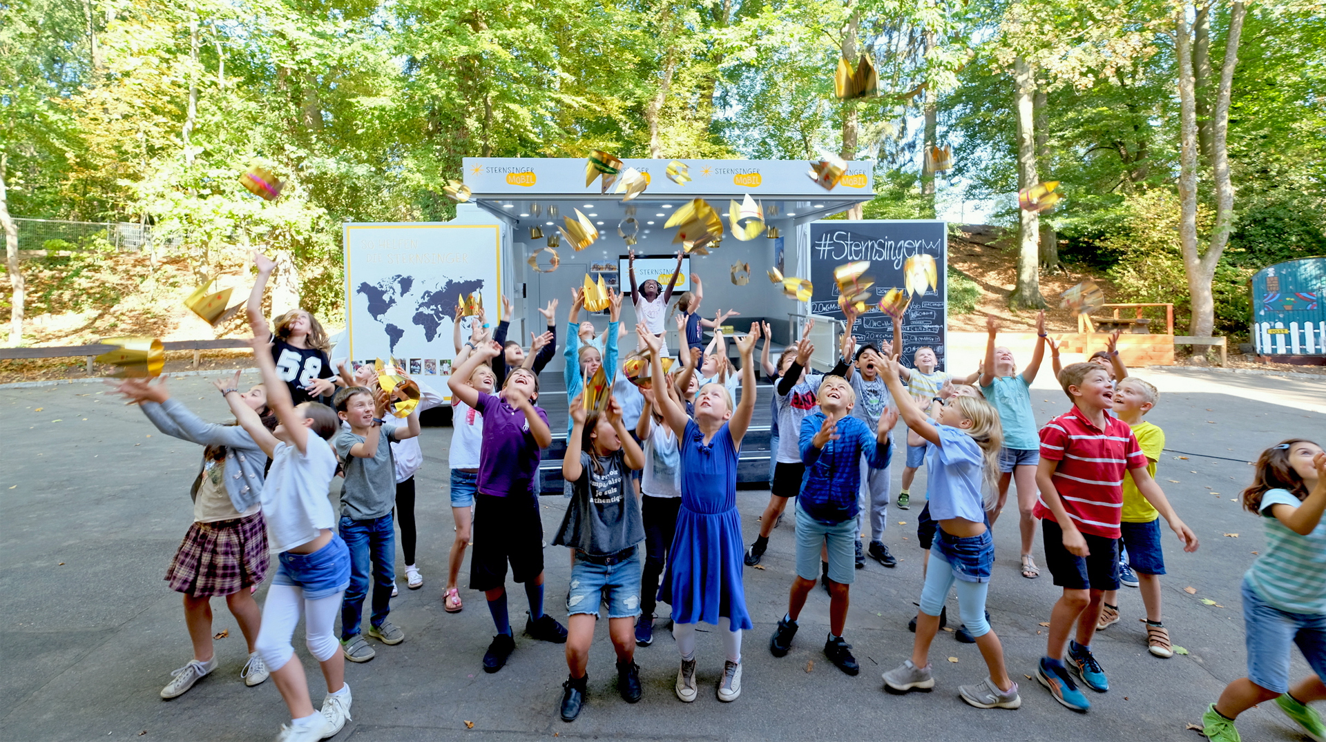 Kinder werfen vor dem Sternsingermobil Kronen in die Luft