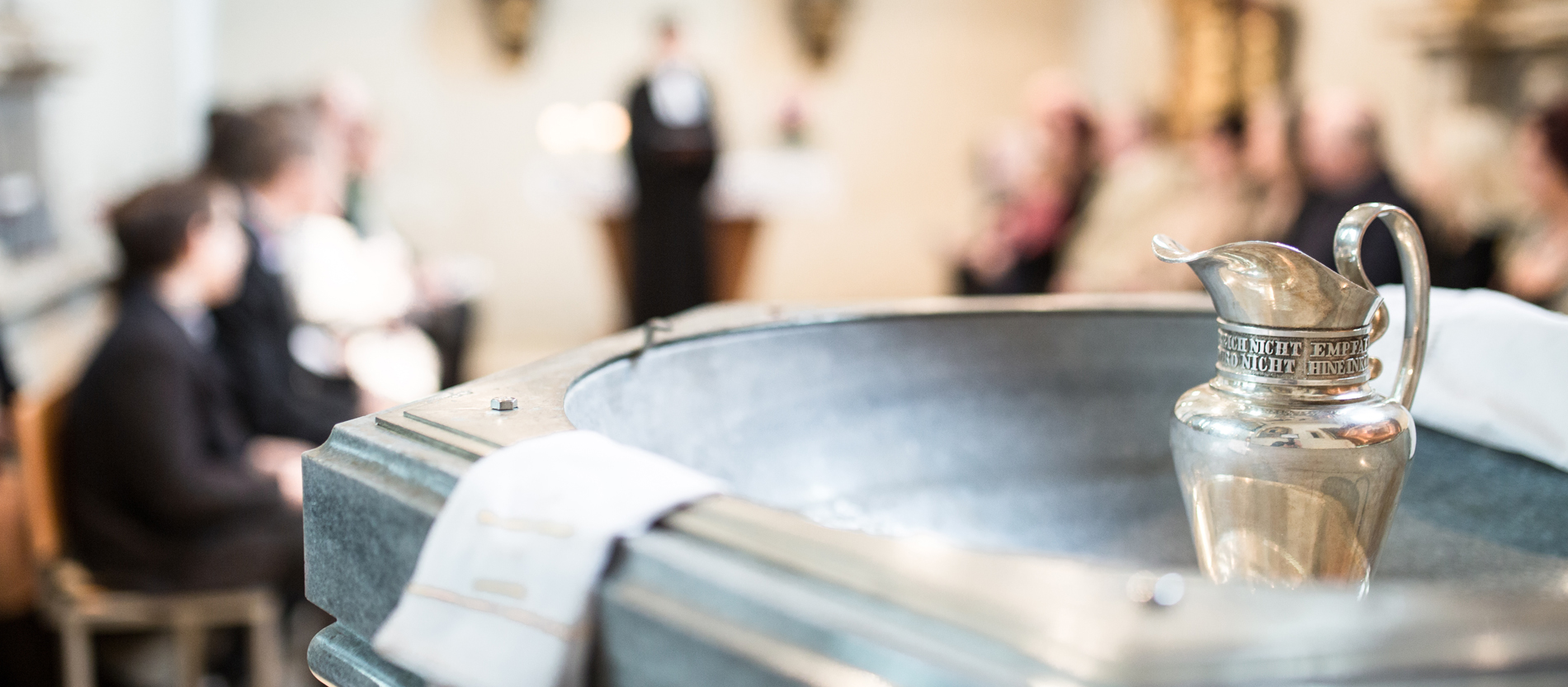 A baptismal font in a church, with the congregation in the background