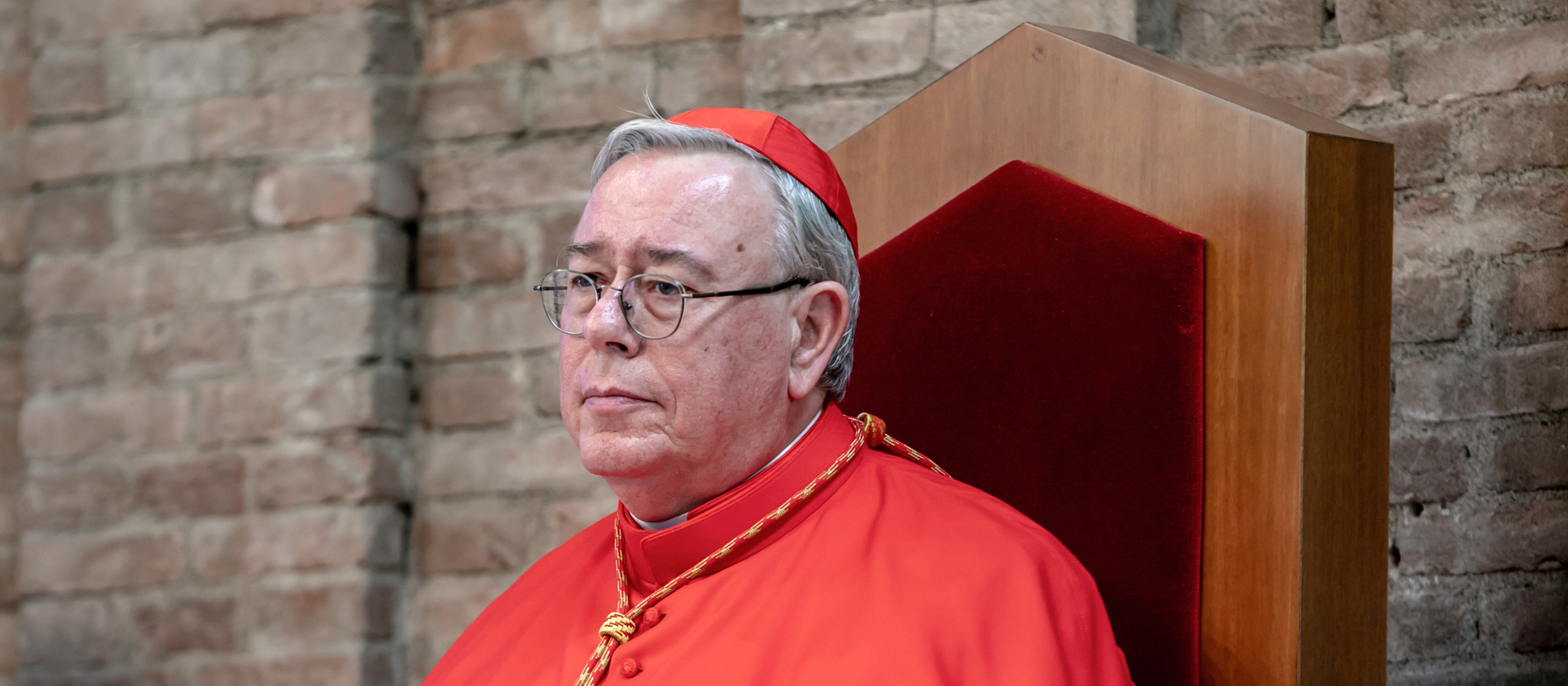 Jean-Claude Hollerich sits on a bishop's chair in front of a stone wall