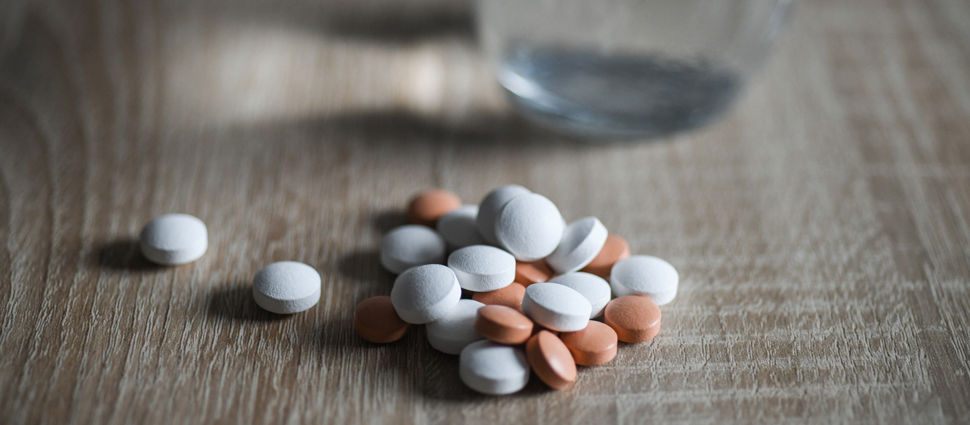 Many tablets lying next to a glass of water on a wooden table