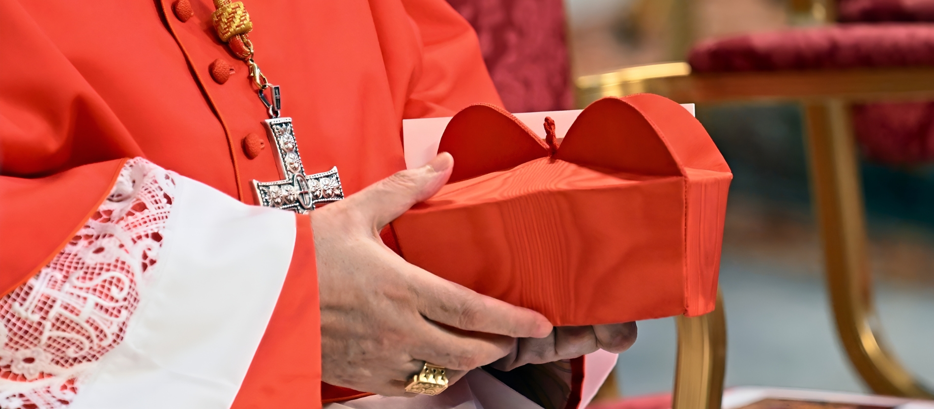 A cardinal holds a red biretta in his hand