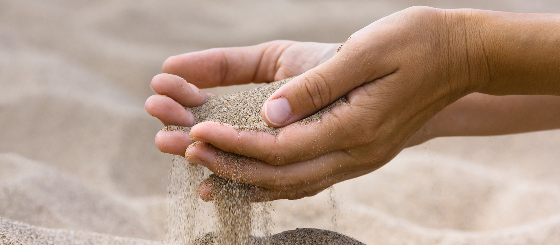Sand läuft zwischen den Fingern einer Frau hindurch