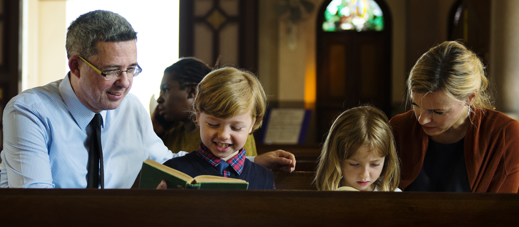 Ein Vater und eine Mutter haben ihre Kinder zwischen sich in die Kirchenbank gesetzt.